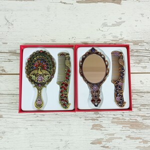 May include: Two sets of decorative mirrors and combs in red boxes. One set features a peacock design, with a round mirror and comb. The other set has an oval mirror and comb. The sets are in a red box.