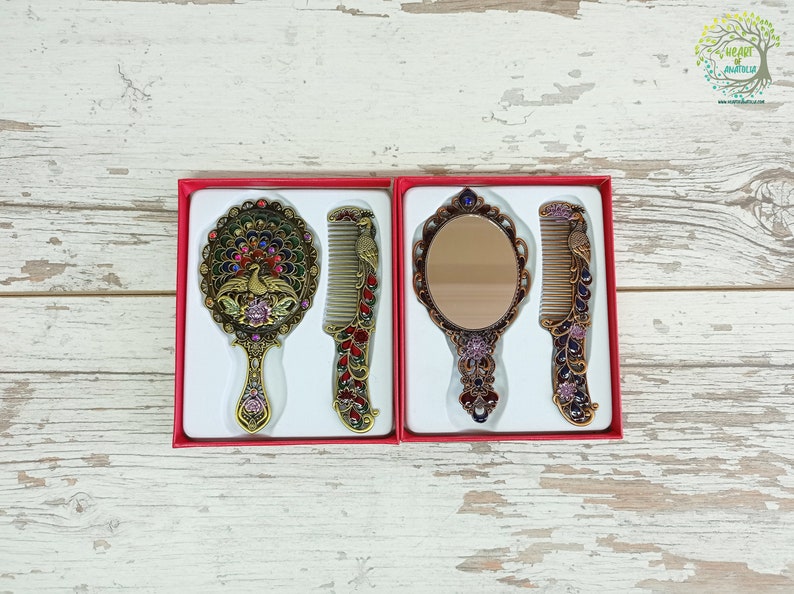 May include: Two sets of decorative mirrors and combs in red boxes. One set features a peacock design, with a round mirror and comb. The other set has an oval mirror and comb. The sets are in a red box.