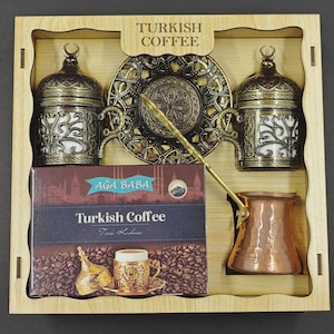 May include: A wooden gift box containing two ornate antique brass-colored coffee cups with lids, a matching decorative saucer, a copper-colored coffee pot, and a rectangular box labeled Turkish Coffee with an image of coffee beans.