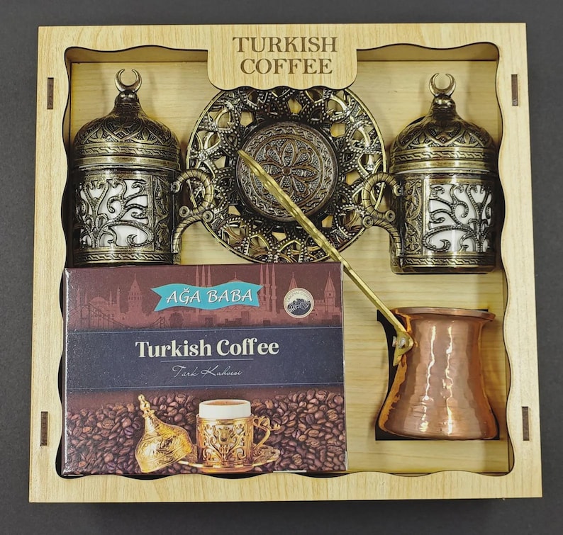 May include: A wooden gift box containing two ornate antique brass-colored coffee cups with lids, a matching decorative saucer, a copper-colored coffee pot, and a rectangular box labeled Turkish Coffee with an image of coffee beans.