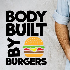 May include: Black and white text on a gray background reads "Body Built By Burgers". A cartoon image of a hamburger with lettuce, tomato, cheese, and a sesame seed bun is below the text.