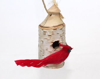 May include: A red cardinal bird ornament perched on a birch bark birdhouse with a rope hanger.