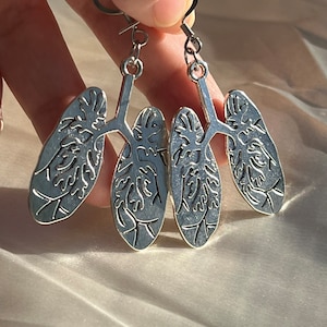 May include: A pair of silver earrings shaped like human lungs. The earrings are detailed with a realistic depiction of the lungs' internal structure.