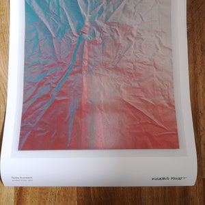May include: A close-up of a crumpled piece of fabric with a blue and pink gradient. The fabric is textured and has a wrinkled appearance. The text "MODENA MUSSET" is written in black ink at the bottom of the image.