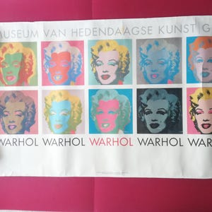 Puede incluir: Un póster con una cuadrícula de retratos de Marilyn Monroe en diversos colores vibrantes. La palabra "WARHOL" se repite debajo de cada imagen, con el texto "MUSEUM VAN HEDENDAAGSE KUNST GENT" en la parte superior. La obra está sobre un fondo rosa.