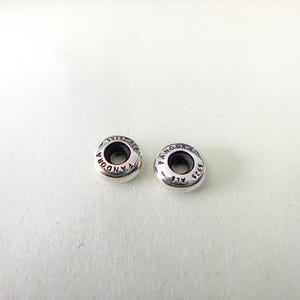 May include: Two round, silver-colored metal spacer beads with a smooth, polished finish. Each bead features the engraved text PANDORA and S925 ALE along the top surface, surrounding a central circular opening for threading onto a bracelet.