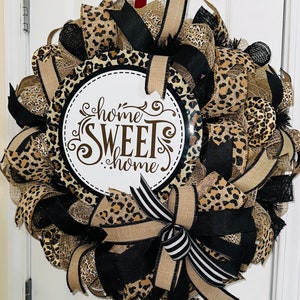 Op de afbeelding: Een krans met luipaardprint met een zwart-wit gestreepte strik. De krans heeft een rond bord in het midden met de tekst "home sweet home".