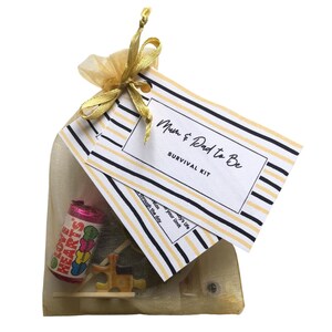May include: A gold organza bag filled with a survival kit for new parents. The kit includes a small bag of Love Hearts sweets, a wooden puzzle, and a card that reads "Mum & Dad to Be Survival Kit".