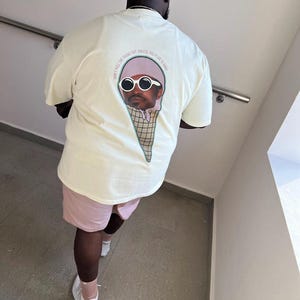 Op de afbeelding: Een wit T-shirt met een afbeelding van een persoon met een zonnebril en een hoed op een ijshoorn. De tekst op het shirt luidt "Don't pull the thangs out, unless you plan to bang."