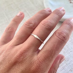 May include: A silver ring featuring a small, elongated, diamond-shaped design. The ring is worn on a finger, highlighting its minimalist style. The ring's band is thin and delicate, and the design is centered. Likely made of sterling silver, it's a simple piece of jewellery.