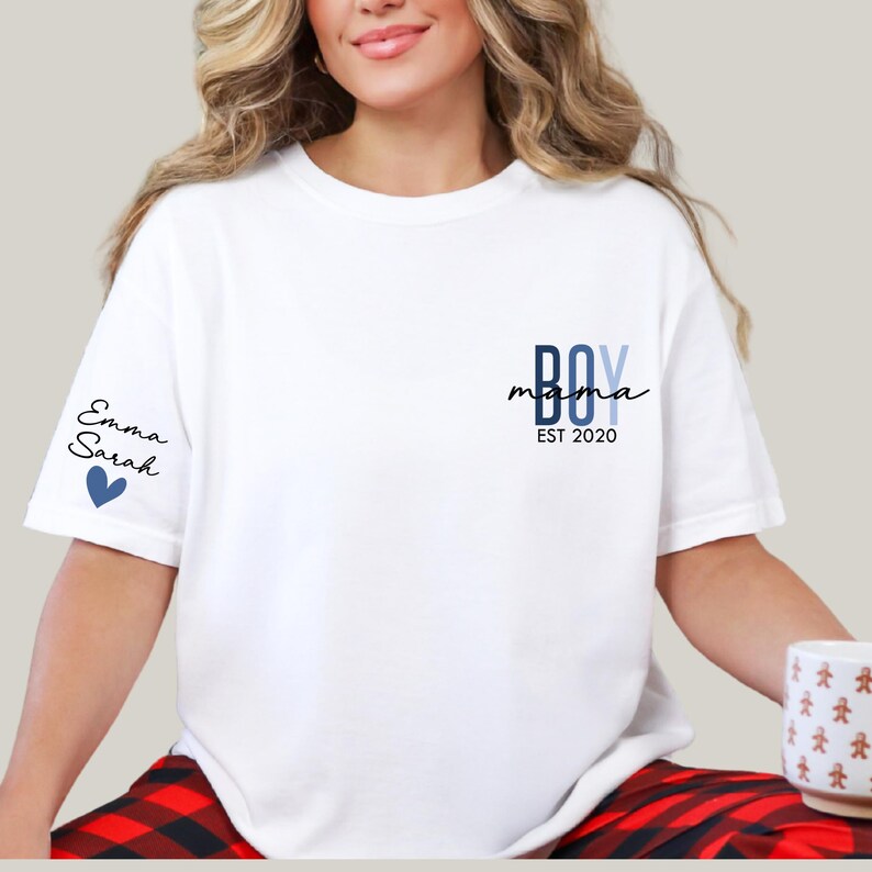 A woman wearing a white t-shirt with a blue logo and text on it, sitting on a red and black plaid blanket.