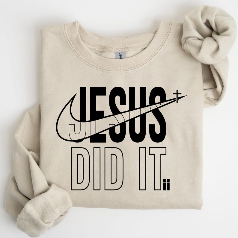 A beige t-shirt with a graphic design featuring the text "JESUS DID IT" and a Nike swoosh logo.
