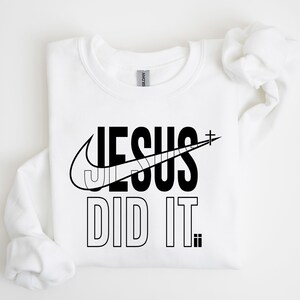 A white t-shirt with a graphic design featuring the text "JESUS DID IT" and a Nike swoosh logo.