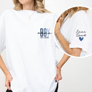 A woman wearing a white t-shirt with a personalized design on the left side.