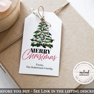 May include: A white gift tag with a watercolor Christmas tree design, red berries, and the words "MERRY Christmas" in black and red. The tag is tied with twine and rests on a wrapped gift. The text "From, The Robertson Family" is also present.