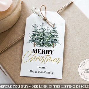May include: A white gift tag with a watercolor illustration of snow-covered pine trees. The text "Merry Christmas" is written in gold script with "From, The Wilson Family" below. The tag is tied with twine and is ready to be attached to a gift.