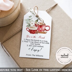 May include: A gift tag with a watercolor illustration of two red mugs with marshmallows and a cinnamon stick. The tag reads "You're the Bomb" with instructions and "Enjoy!" at the bottom. The gift is wrapped in brown paper.