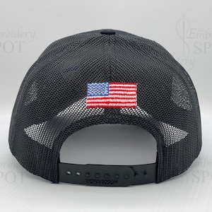 May include: Black mesh trucker hat with a small American flag patch on the back. The hat has an adjustable strap with the word "Richardson" printed on it.