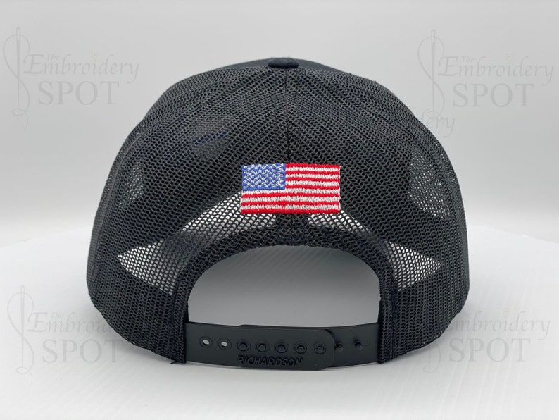 May include: Black mesh trucker hat with a small American flag patch on the back. The hat has an adjustable strap with the word "Richardson" printed on it.