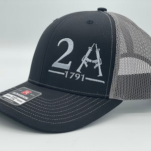 May include: A black and grey trucker hat with a white embroidered design that says "2A -1791" with two stylized rifles.