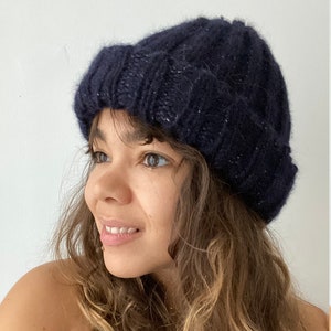 May include: A dark blue knit beanie with a subtle sparkle. The beanie is made of a soft, fuzzy yarn and has a slouchy fit.