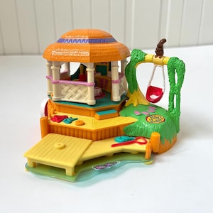 May include: A vintage Polly Pocket playset with a gazebo, swing set, and small table. The playset is mainly orange, yellow, and green, with a red swing and pink and blue accents. The gazebo has a thatched roof, and the set is made of plastic.