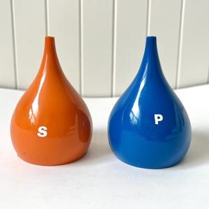 Peut inclure: Une paire de salières et poivrières en forme de goutte d'eau. L'une est orange avec un "S" blanc, l'autre est bleue avec un "P" blanc. Les salières et poivrières ont une finition brillante et un sommet étroit et pointu.