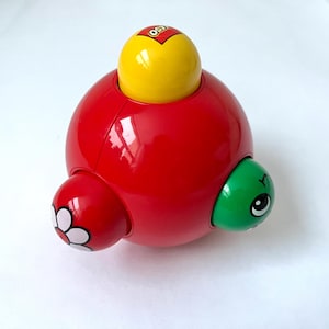 Pode incluir: Um brinquedo de plástico vermelho, amarelo e verde com um desenho de flor. O brinquedo tem a forma de uma esfera com três seções de cores diferentes. O brinquedo é feito pela LEGO.