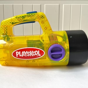 Könnte beinhalten: Eine gelbe Playskool Wasserpistole aus Plastik mit einem violetten Knopf und einer schwarzen Düse.