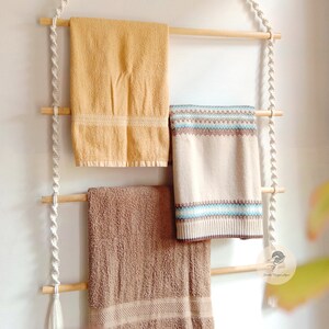 Peut inclure: Une suspension murale en macramé blanche avec trois chevilles en bois et trois serviettes suspendues. Les serviettes sont jaunes, brunes et blanches avec un motif bleu et brun.