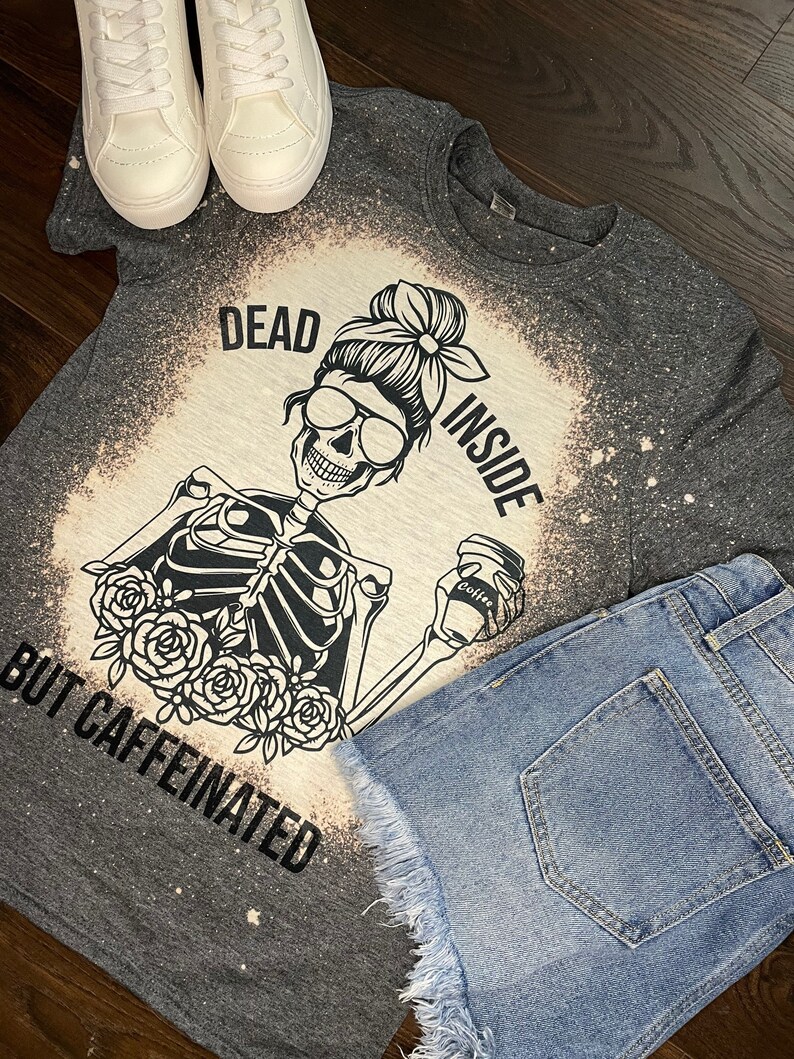 May include: A gray t-shirt with a bleached design featuring a skeleton holding a coffee cup. The text on the shirt reads "Dead Inside But Caffeinated".