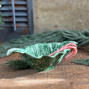 May include: A green ceramic bowl shaped like a cabbage leaf with two red and white candy canes inside.