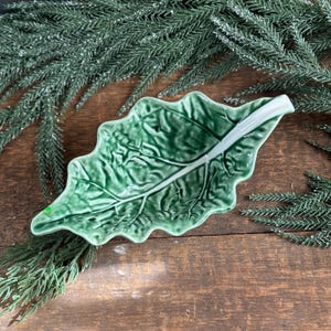 May include: A green ceramic serving dish shaped like a cabbage leaf. The dish has a textured surface and a white rim.