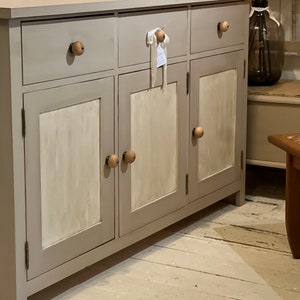 May include: A gray wooden cabinet with three drawers and three doors. The cabinet has a distressed white paint finish and wooden knobs.
