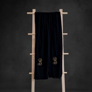 May include: Black throw blanket with gold embroidered initials "BB" hanging on a wooden ladder.