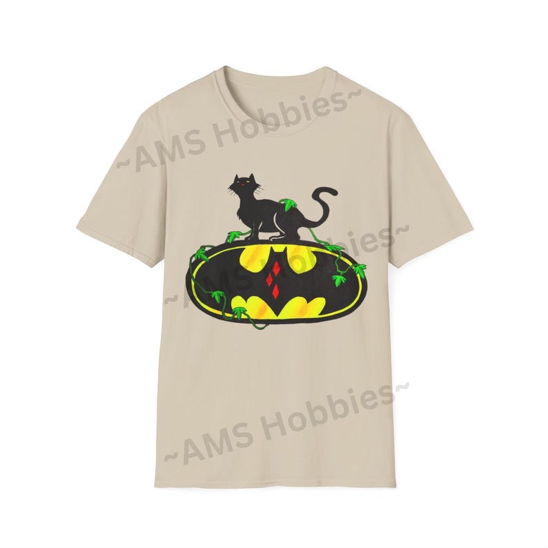 May include: A beige t-shirt with a black cat sitting on a yellow and black Batman logo with green vines. The logo has a red diamond in the center.