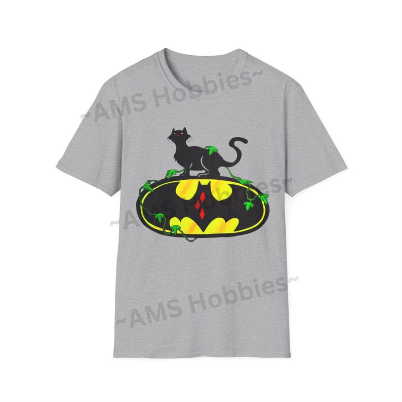 May include: A gray t-shirt with a black cat sitting on a yellow and black Batman logo with green vines. The logo has a red diamond in the center.