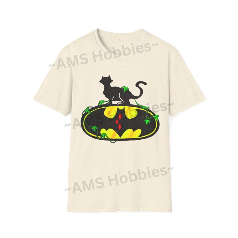 May include: A beige t-shirt with a black cat sitting on top of a yellow Batman logo with green vines. The logo has a red diamond in the center. The text "AMS Hobbies" is printed on the shirt.