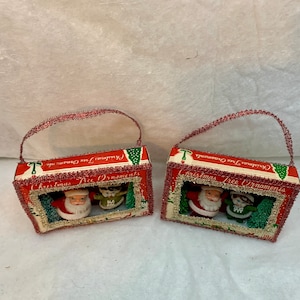 May include: Two vintage Christmas tree ornaments in boxes with red and green trim. The boxes have a red and white background with the text "Christmas Tree Ornaments".