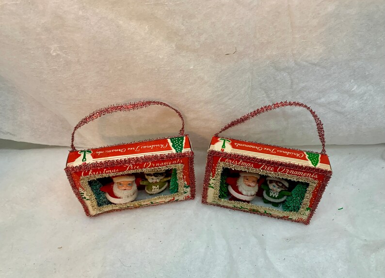 May include: Two vintage Christmas tree ornaments in boxes with red and green trim. The boxes have a red and white background with the text "Christmas Tree Ornaments".