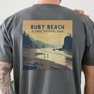 May include: Two people wearing charcoal grey t-shirts. The back of the t-shirt on the left features a vintage-style illustration of Ruby Beach, Olympic National Park. The front of the t-shirt on the right has the text "Ruby Beach" embroidered in black.