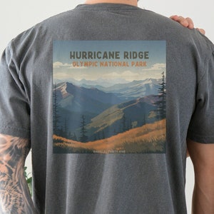 May include: Two people wearing charcoal grey t-shirts. The person on the left has a graphic on the back of their shirt that says "Hurricane Ridge Olympic National Park" with a scenic mountain view. The person on the right has a small graphic on the back of their shirt that says "Hurricane Ridge Olympic National Park".