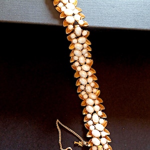 May include: A gold-toned bracelet featuring a leaf design with oval, white gemstones. The bracelet has a delicate chain and clasp. The gemstones are arranged in a repeating pattern along the length of the bracelet.