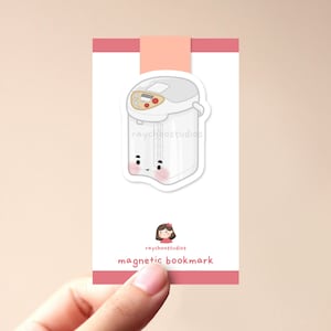 Op de afbeelding: Witte magnetische bladwijzer met een cartoonillustratie van een witte waterkoker met een schattig gezicht. De bladwijzer heeft de tekst "raychoostudios magnetic bookmark" erop gedrukt.