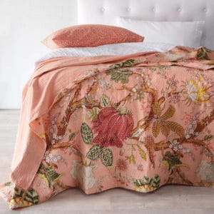 May include: A peach-coloured floral quilt with a detailed botanical design in red, green, and brown. The quilt is draped over a bed, with a matching peach pillow and white bedding visible.