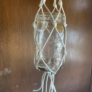 May include: White macrame plant hanger with a glass jar. The jar has a wide mouth and the text "WIDE MOUTH" is visible on the jar.