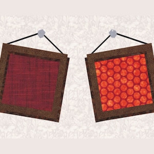 May include: Two framed pieces of fabric hanging on a wall. The fabric on the left is a solid dark red color. The fabric on the right has a red and orange polka dot pattern.