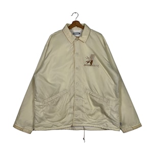 Puede incluir: Una chaqueta de entrenador de color crema con un logotipo marrón que dice "DVLCNTRL.FTR."