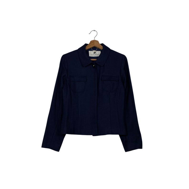 May include: A navy blue blazer with a collared neckline and two front pockets. The blazer is hanging on a wooden hanger against a white background. The blazer has a button closure.