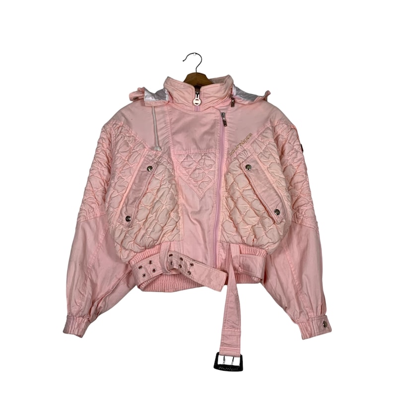 May include: A pink quilted jacket with a zip closure, a belt with a buckle, and a hood. The jacket has a quilted design and multiple pockets.